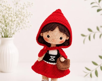 Peut inclure: Une poupée crochetée à la main représentant un personnage aux cheveux brun foncé, portant une cape à capuche rouge vif, un corsage noir avec des détails de laçage blancs et une jupe rouge. La poupée a de petits yeux noirs et un panier marron.