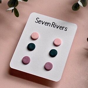 May include: A set of six polymer clay earrings in three colors: pink, dark pink, and black. The earrings are displayed on a white card with the text "Seven Rivers".