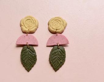 May include: A pair of dangle earrings with a yellow rose, pink half-circle, and green leaf charm.