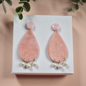May include: Pink teardrop shaped earrings with gold flecks and white pearl accents.