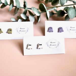 Op de afbeelding: Drie sets met spookvormige oorbellen op witte kaartjes. De oorbellen zijn gemaakt van polymer clay en verkrijgbaar in goudglitter, paars en wit.