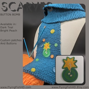 May include: A teal knitted scarf with a button and patch design. The scarf features a star and button patch, along with various colorful buttons. The text "BUTTON BOMB" is visible, along with "Available in: Dark Teal, Bright Peach".