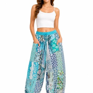 Op de afbeelding: Een wit mouwloos crop-topje gecombineerd met een losvallende, enkelbroek met een patchwork-ontwerp in diverse tinten blauw, turquoise en wit. De broek heeft een elastische tailleband met een trekkoord en twee zijzakken.