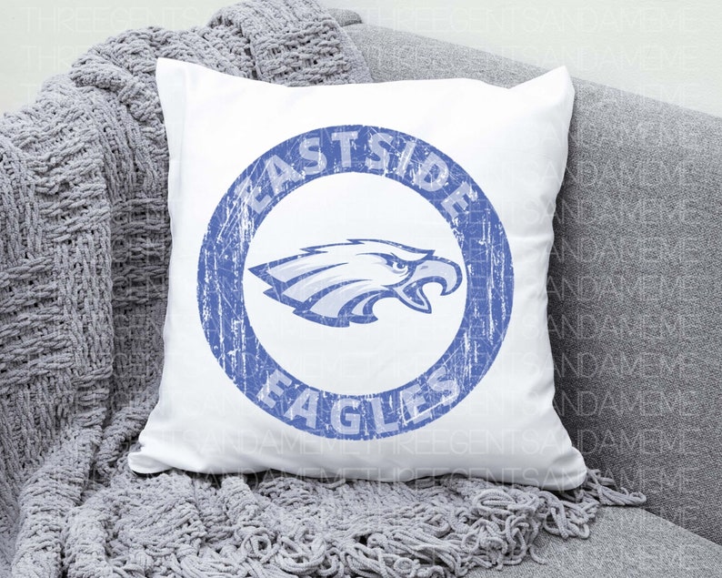 K&ouml;nnte beinhalten: Ein wei&szlig;es Kissen mit einem blauen Kreisdesign, auf dem "Eastside Eagles" steht und ein blauer Adler im Kreis abgebildet ist.