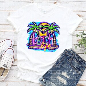 Pu&ograve; includere: Maglietta bianca con un design grafico colorato di palme e il testo "Beach Life".