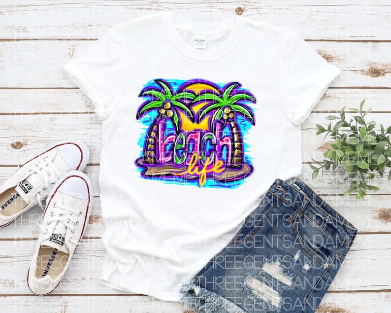 Pu&ograve; includere: Maglietta bianca con un design grafico colorato di palme e il testo "Beach Life".