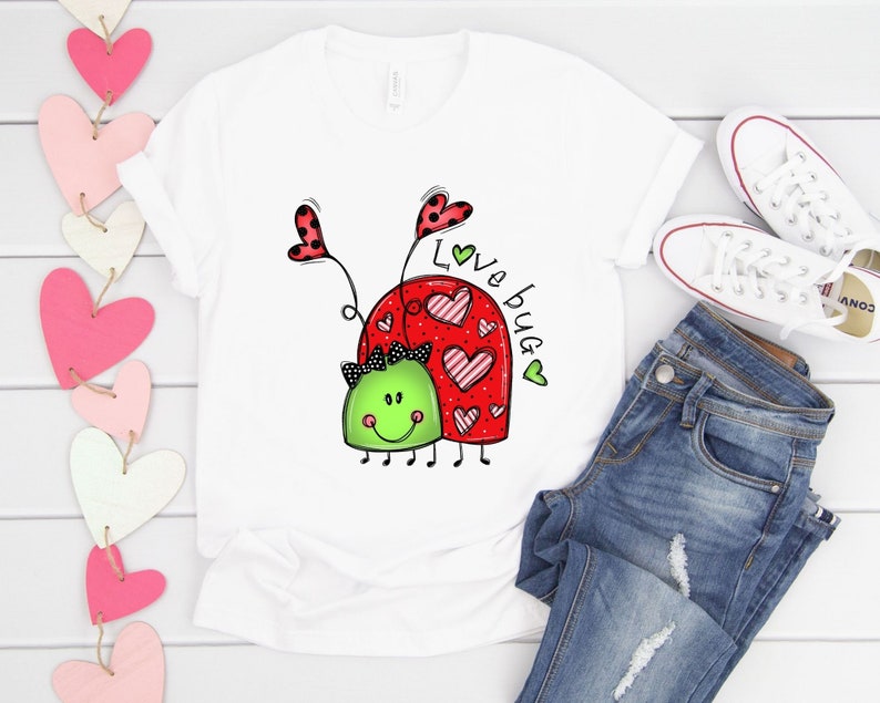 K&ouml;nnte beinhalten: Wei&szlig;es T-Shirt mit einem roten Marienk&auml;fer-Design und dem Text "Love Bug" in schwarzer und gr&uuml;ner Schrift.