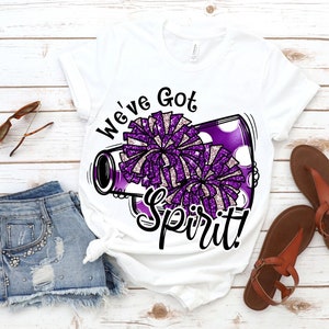 Op de afbeelding: Wit T-shirt met een paarse en witte cheerleading-megaphone afbeelding en de tekst "We've Got Spirit!"