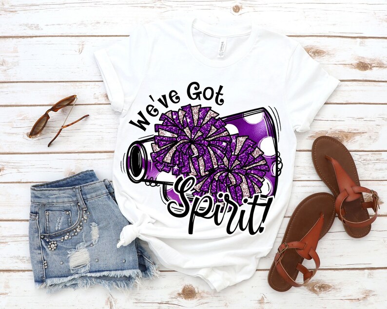 Op de afbeelding: Wit T-shirt met een paarse en witte cheerleading-megaphone afbeelding en de tekst "We've Got Spirit!"