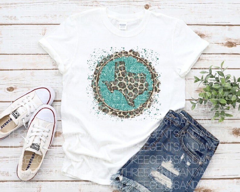 May include: White t-shirt with a turquoise and brown leopard print Texas state design. The design is surrounded by white paint splatters.