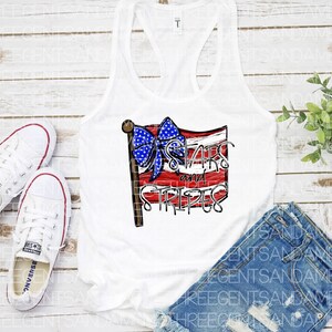 May include: White tank top with a red, white, and blue American flag design. The flag has a blue bow on top and the text "Stars and Stripes" written on it.