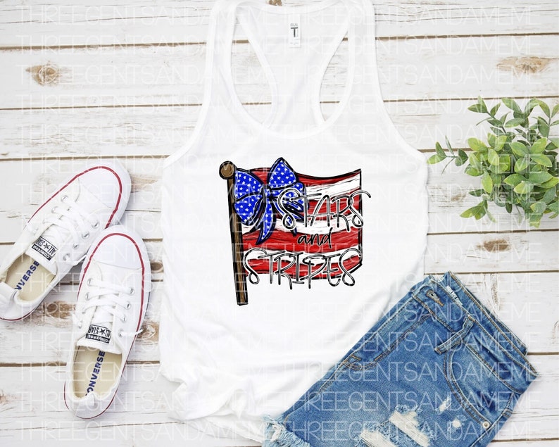 May include: White tank top with a red, white, and blue American flag design. The flag has a blue bow on top and the text "Stars and Stripes" written on it.