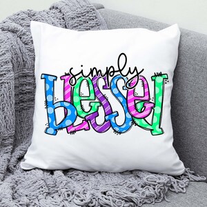 May include: White pillow with the words "simply blessed" in colorful, patterned letters. The letters are outlined in black and have a playful, hand-drawn style.