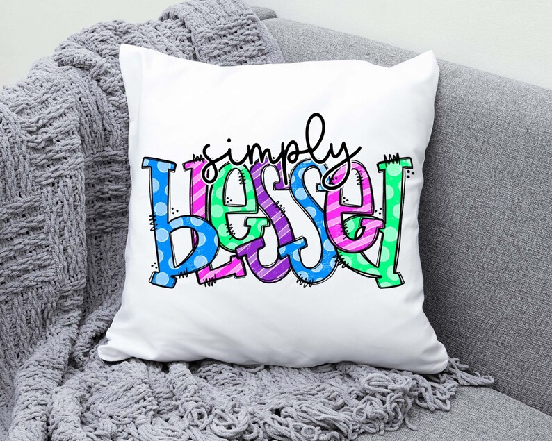 May include: White pillow with the words "simply blessed" in colorful, patterned letters. The letters are outlined in black and have a playful, hand-drawn style.