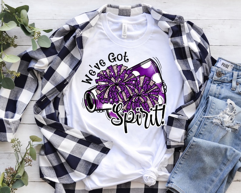 Op de afbeelding: Wit T-shirt met een paarse en witte megafoon met pompoenen en de tekst "We've Got Spirit!"