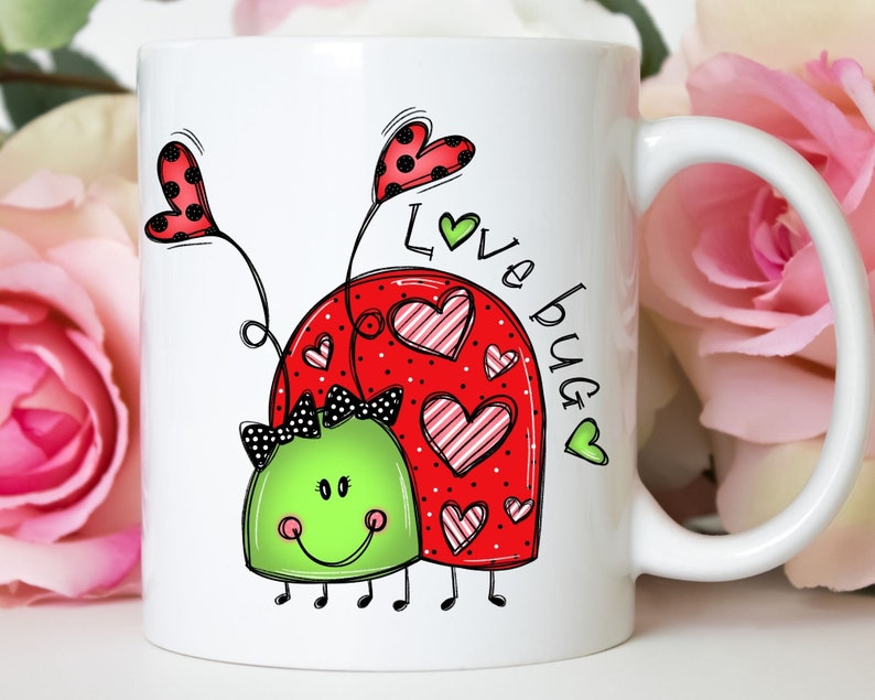 K&ouml;nnte beinhalten: Wei&szlig;e Keramiktasse mit einem roten Marienk&auml;fer-Design und dem Text "Love bug" in schwarzer und gr&uuml;ner Schrift. Der Marienk&auml;fer hat schwarze Punkte und rosa-wei&szlig; gestreifte Herzen.
