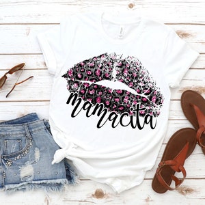 Pu&ograve; includere: Maglietta bianca con un design a labbra con stampa leopardata rosa e nera e la parola "mamacita" stampata sotto.