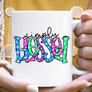 May include: White ceramic mug with a colorful design that says "simply blessed".