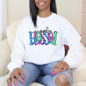 May include: White sweatshirt with the text "simply blessed" in colorful letters with polka dots and stripes.