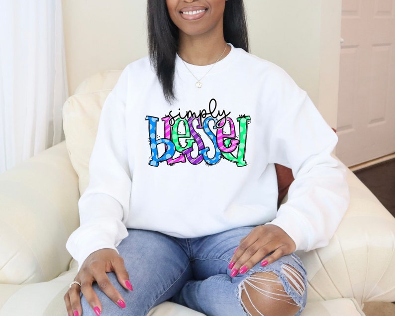 May include: White sweatshirt with the text "simply blessed" in colorful letters with polka dots and stripes.