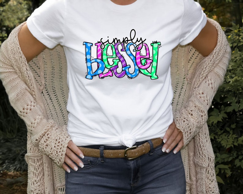 May include: A white t-shirt with the text "simply blessed" in colorful letters with polka dots and stripes.