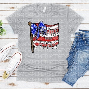 May include: Gray V-neck t-shirt with a red, white, and blue American flag design. The flag has a blue bow with white stars and the text "Stars and Stripes" written on it.