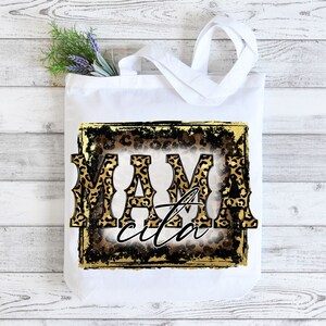 May include: White tote bag featuring a gold and black leopard print design. The text "Mamacita" is written in a bold, black font.
