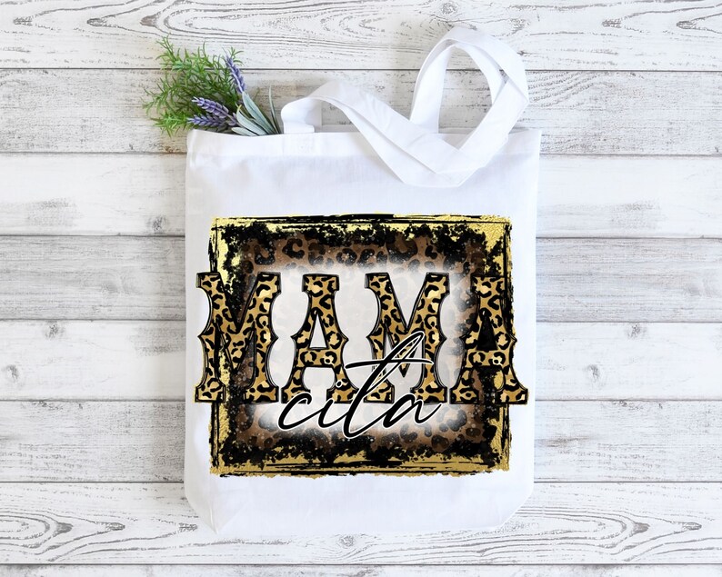 May include: White tote bag featuring a gold and black leopard print design. The text "Mamacita" is written in a bold, black font.