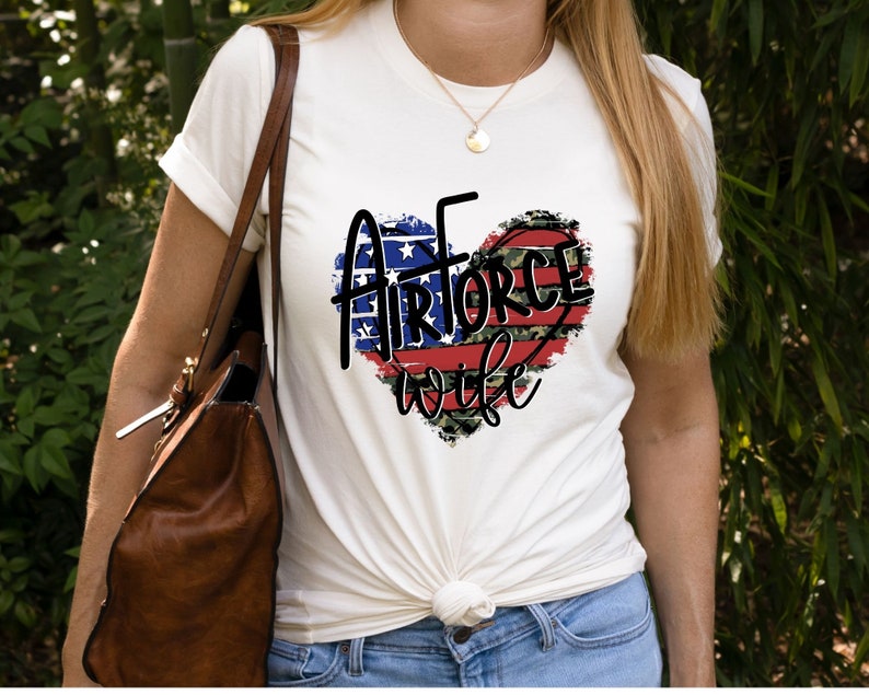 May include: White t-shirt with a red, white, and blue heart design. The heart has the words "Air Force Wife" inside.