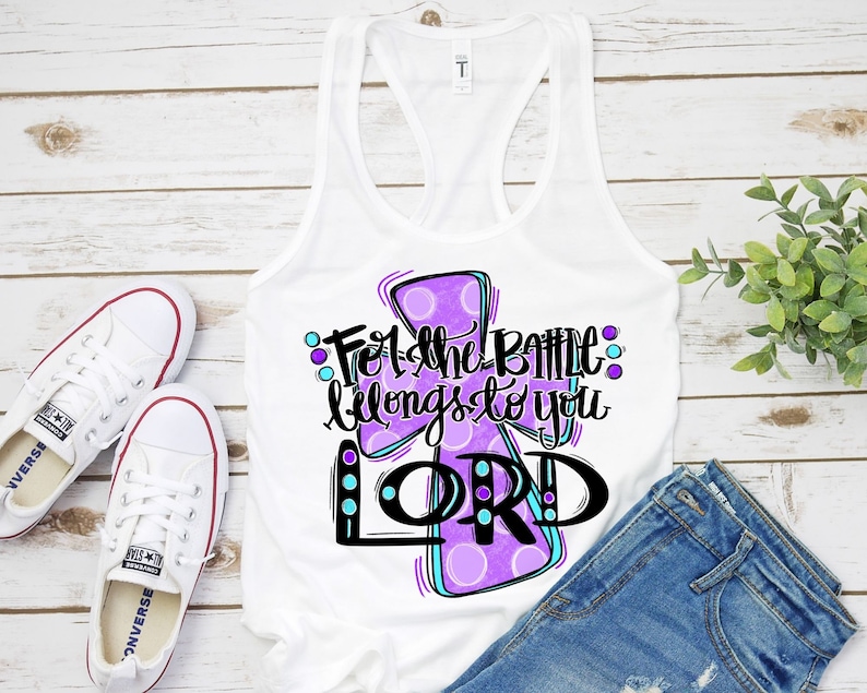 May include: White tank top with a purple and blue cross design. The text "For the battle belongs to you LORD" is written on the cross.