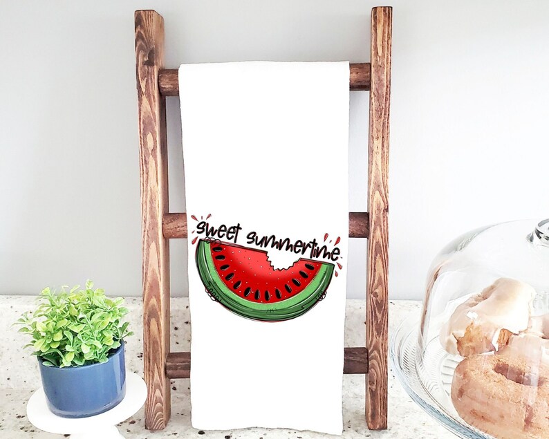 May include: White kitchen towel with a red and green watermelon slice graphic and the text "sweet summertime". The towel is hanging on a wooden ladder.
