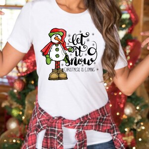 May include: White t-shirt with a snowman graphic and the text "Let it snow" with a smaller text "Christmas is coming".