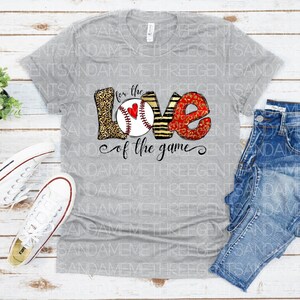 May include: Gray t-shirt with a baseball-themed graphic that says "For the Love of the Game". The graphic features a baseball with a red heart, surrounded by the letters "LOVE" in a leopard print and zebra print.