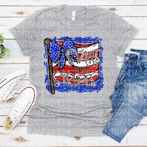 May include: A gray t-shirt with a distressed graphic of a red, white, and blue American flag with a blue bow. The text "Stars and Stripes" is written on the flag.