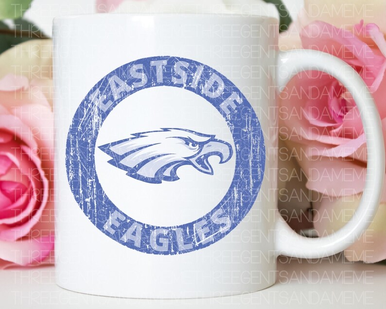 K&ouml;nnte beinhalten: Wei&szlig;e Keramiktasse mit einem blauen und wei&szlig;en, abgenutzten Kreisdesign. Der Kreis zeigt "Eastside Eagles" mit einer blauen Adlergrafik im Inneren.