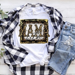 May include: White t-shirt with a gold and black graphic that says "Mamacita" in a leopard print font.