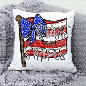 May include: White pillow with a red, white, and blue American flag design. The flag has a blue bow with white stars and the words "Stars and Stripes" written in white.
