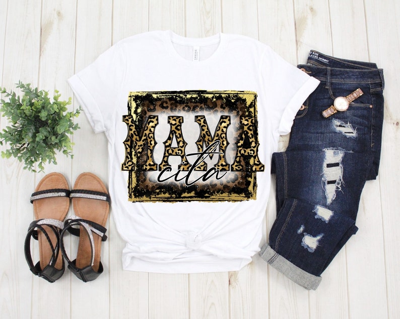 May include: White t-shirt with a gold and black graphic that says "Mamacita" in a leopard print font.