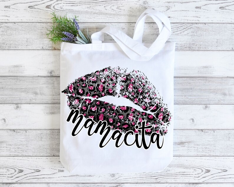 Pu&ograve; includere: Borsa tote bianca con un design a labbra con stampa leopardata nera e rosa e il testo "mamacita" in nero.