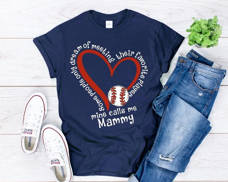 May include: Navy blue t-shirt with a red heart and a baseball graphic. The text on the shirt reads "Some people only dream of meeting their favorite player, mine calls me Mammy".