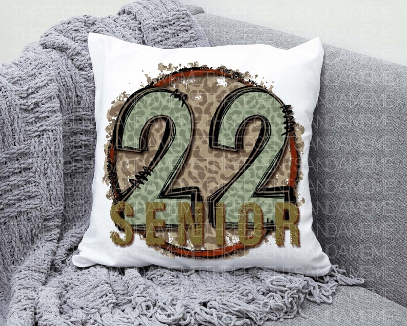 Puede incluir: Almohada blanca con un dise&ntilde;o circular marr&oacute;n y verde. El c&iacute;rculo tiene un patr&oacute;n de estampado de leopardo y el n&uacute;mero 22 en el centro. El texto "Senior" est&aacute; debajo del n&uacute;mero.
