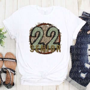 Puede incluir: Camiseta blanca con un gr&aacute;fico circular marr&oacute;n y verde que dice "22 Senior" en una fuente desgastada.