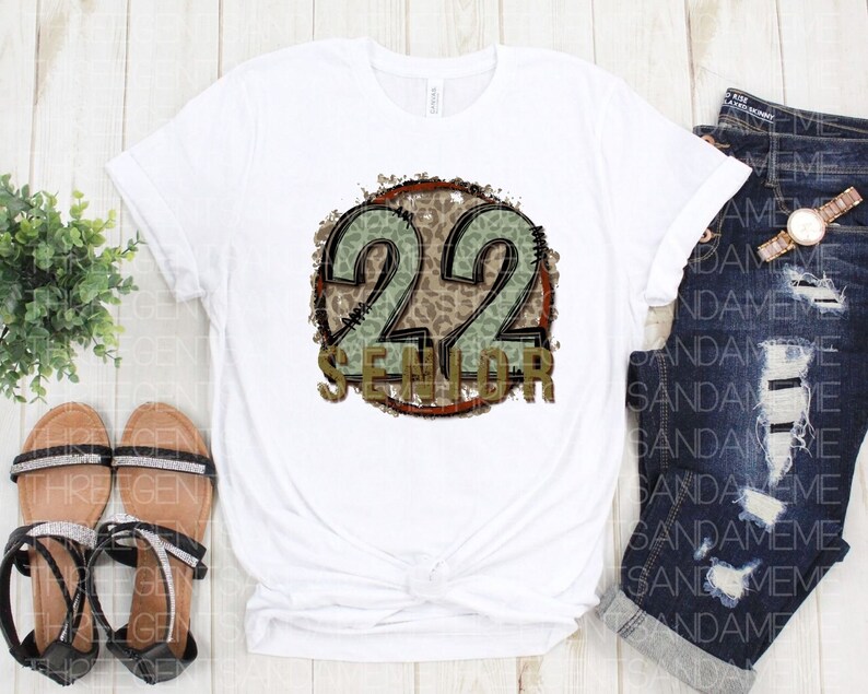 Puede incluir: Camiseta blanca con un gr&aacute;fico circular marr&oacute;n y verde que dice "22 Senior" en una fuente desgastada.