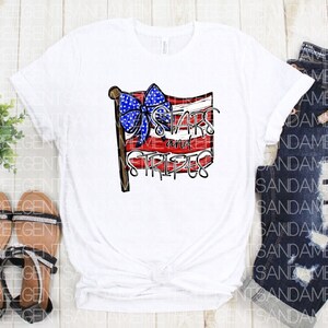 May include: White t-shirt with a red, white, and blue American flag design. The flag has a blue bow on top and the text "Stars and Stripes" underneath.