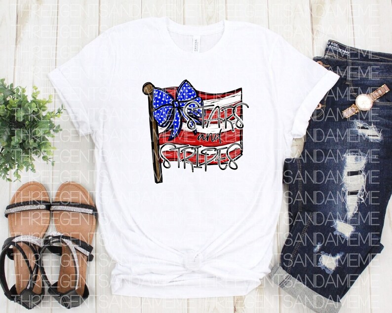 May include: White t-shirt with a red, white, and blue American flag design. The flag has a blue bow on top and the text "Stars and Stripes" underneath.