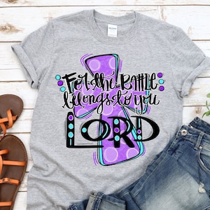 May include: A gray t-shirt with a purple cross and the text "For the battle belongs to you LORD" in black and blue lettering.