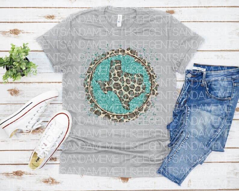 May include: A gray t-shirt with a turquoise and brown graphic of the state of Texas with a leopard print design. The graphic has a distressed look with white paint splatters.