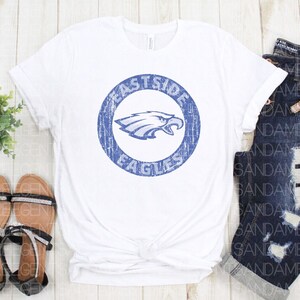 K&ouml;nnte beinhalten: Wei&szlig;es T-Shirt mit einem blauen, abgenutzten Kreis-Motiv, das einen Adler und den Text "Eastside Eagles" zeigt.