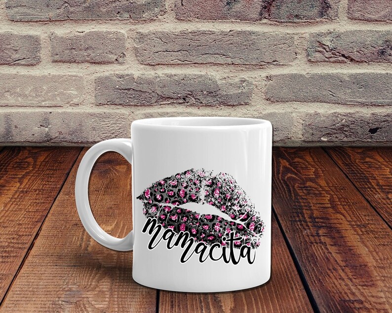 Pu&ograve; includere: Tazza in ceramica bianca con un design a labbra con stampa leopardata nera e rosa e la parola "mamacita" stampata sotto.