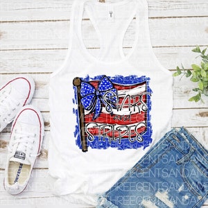May include: White tank top with a red, white, and blue American flag design. The flag has a blue bow on top and the text "Stars and Stripes" in white letters.